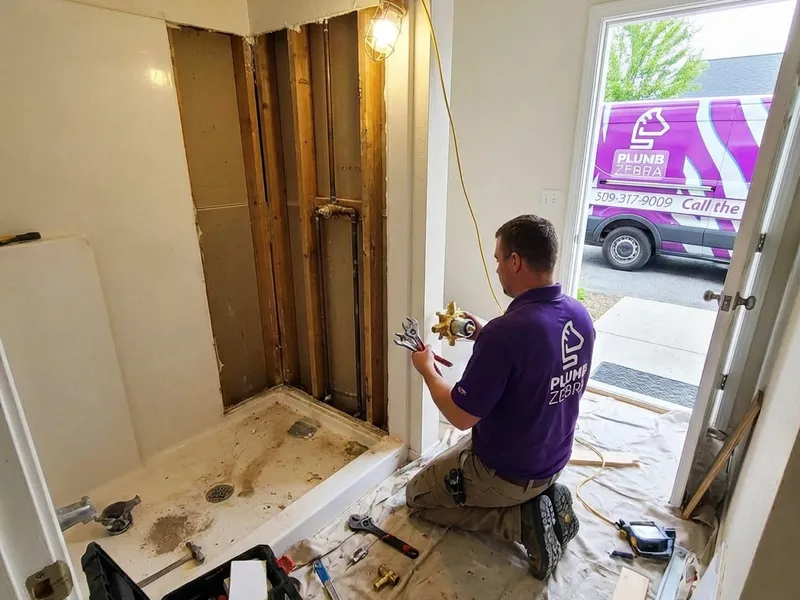 Professional plumber installing modern walk-in shower with glass doors and tile work